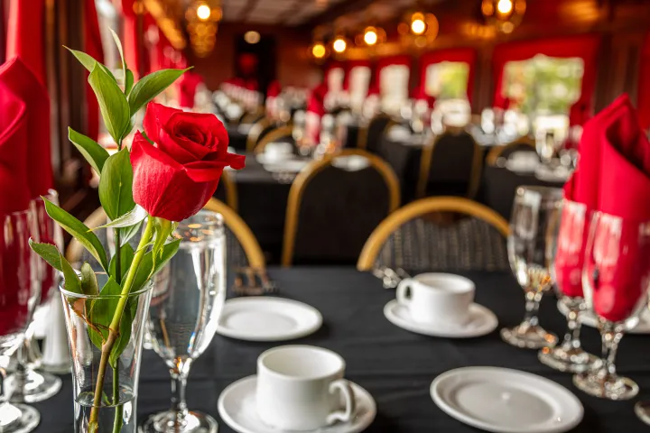 Close-up of a red rose in a vase on a black tablecloth in an elegant dining setting.