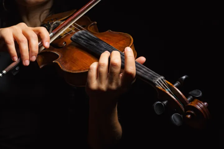 Close-up of hands playing a violin against a dark background.
