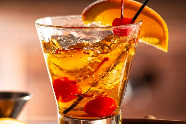 Cocktail with orange slice, cherry, and straw on wooden board.