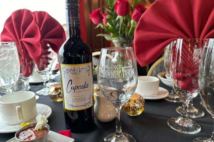 Table setting with wine bottle, glasses, red napkins, roses, and shrimp cocktail on a black tablecloth.