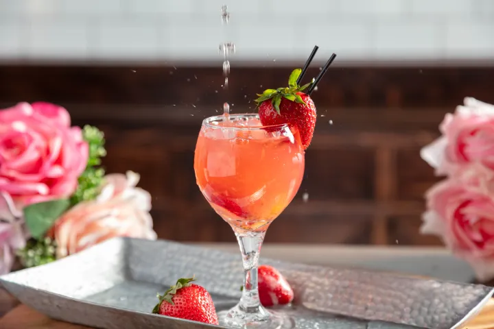 Pink cocktail in glass with strawberries and pink roses on tray.
