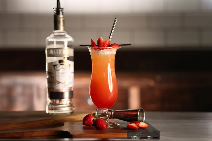 Tropical cocktail with strawberries and bottle on a bar counter.