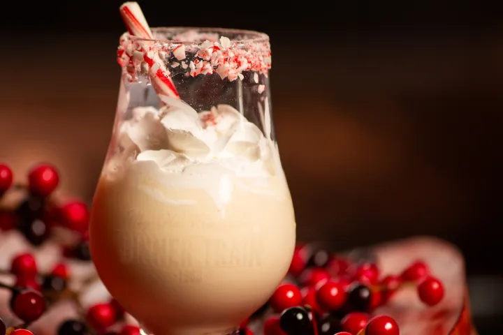 Peppermint cocktail with whipped cream in a festive glass, surrounded by red berries on a wooden surface.