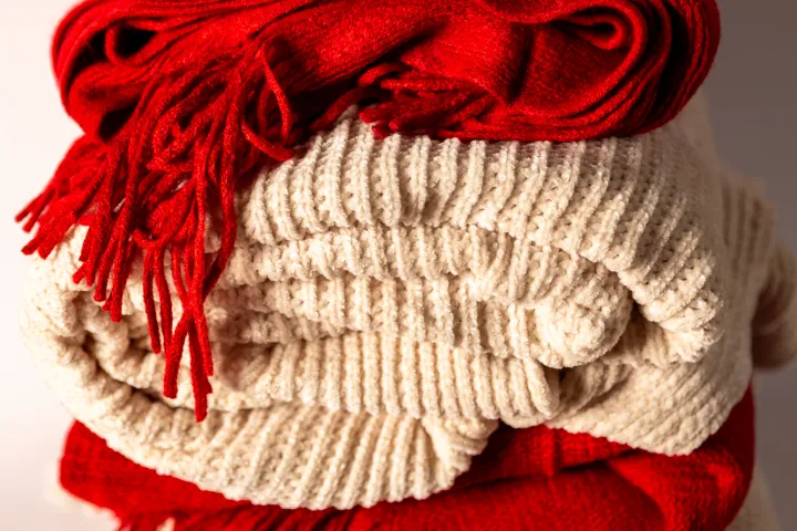 Stack of folded red and white knitted blankets with fringes.