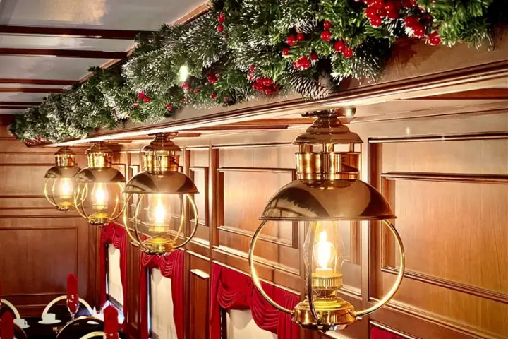 Elegant brass lamps and Christmas garland decorate a wooden-paneled room with red curtains.