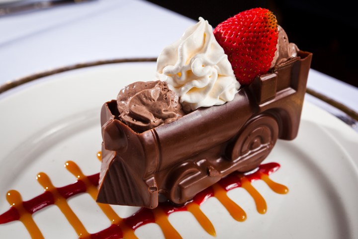 Chocolate train with cream and a strawberry on a decorated plate.