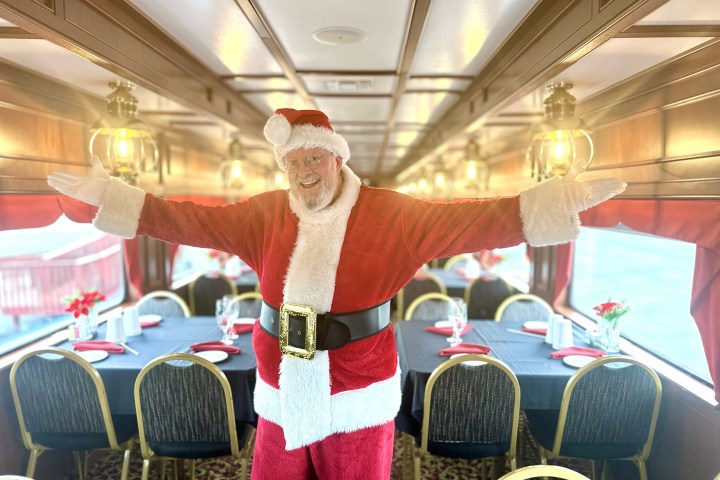 Santa posing in festive train dining car with tables set.