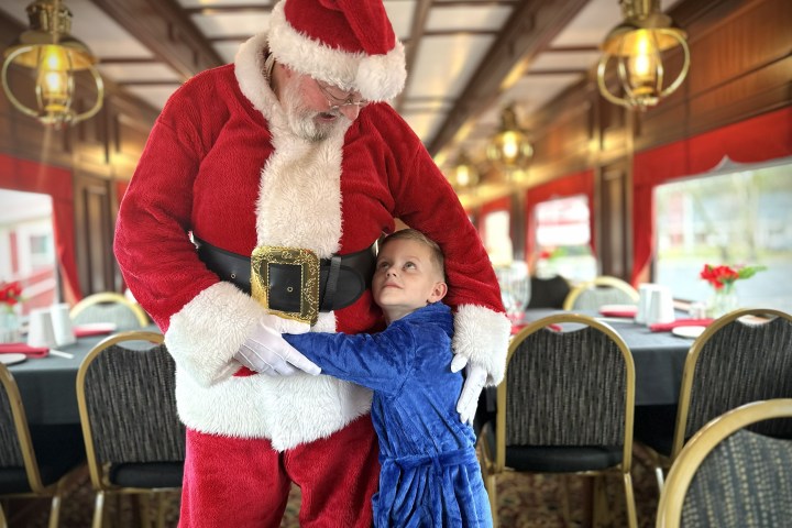 Child in blue robe hugging Santa in a festive room.